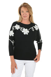 Woman wearing a black sweater with white floral patterned embroidery on a white background.