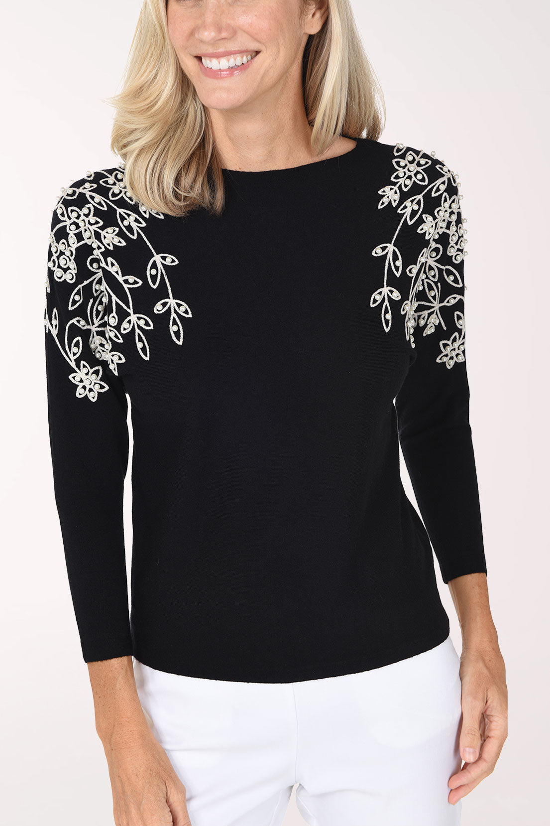 Woman wearing a black 3/4 sleeve sweater with a white pearl embroidery on the shoulders