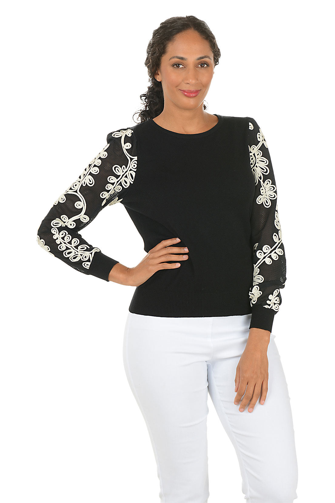 Woman wearing a black top with white embroidery on sleeves against a white background.