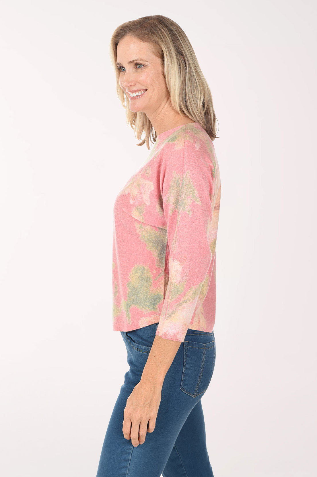 Woman wearing a pink tie-dye shirt and blue jeans on a white background
