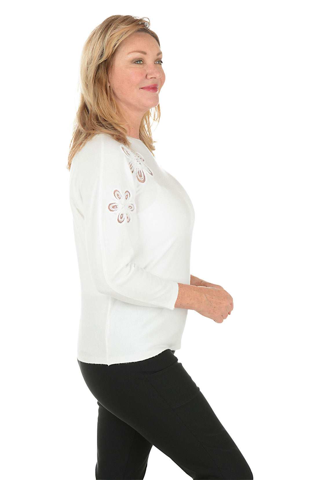 Woman wearing a white sweater with decorative cut-out patterns on a white background. Side shot.