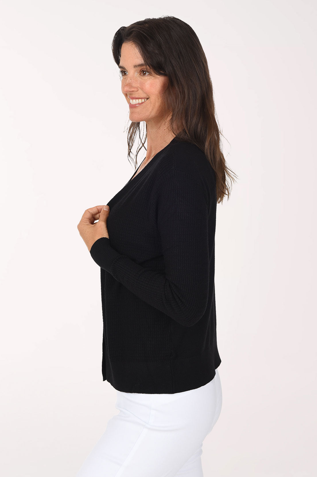 Side view of the black textured cardigan, showing the long fitted sleeves and ribbed hem resting at the hip