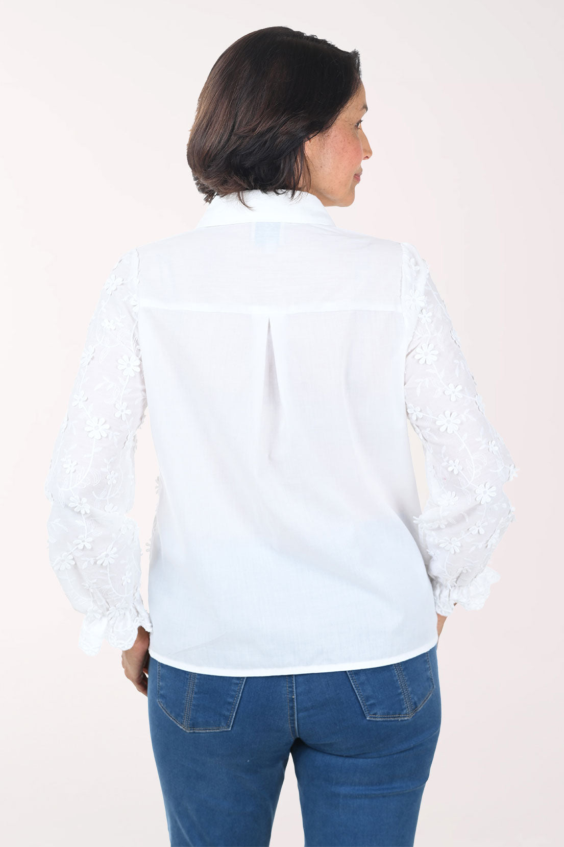 Woman wearing a white patterned shirt and blue pants on a white background