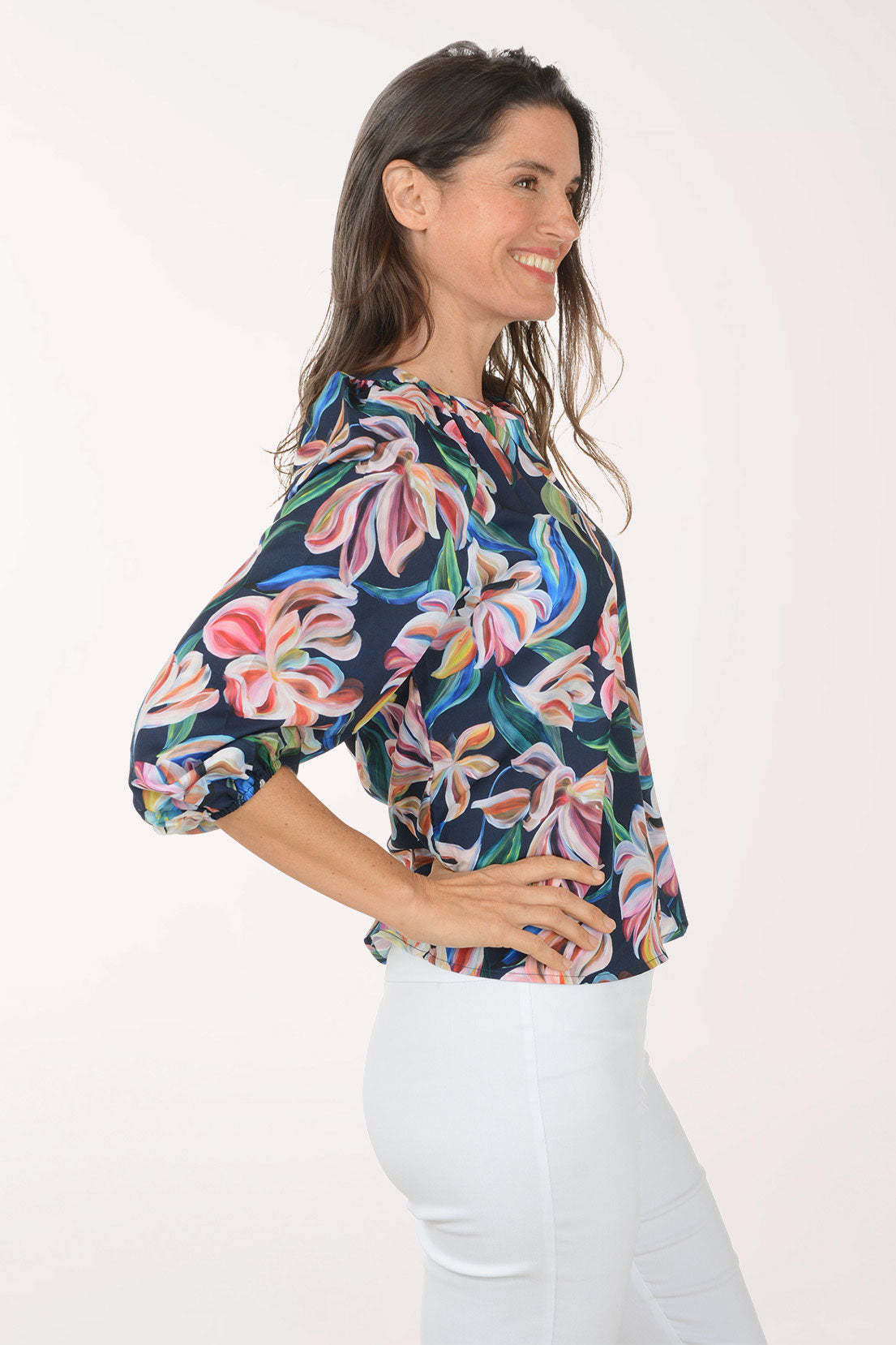 Woman wearing a colorful floral blouse with white pants on a white background