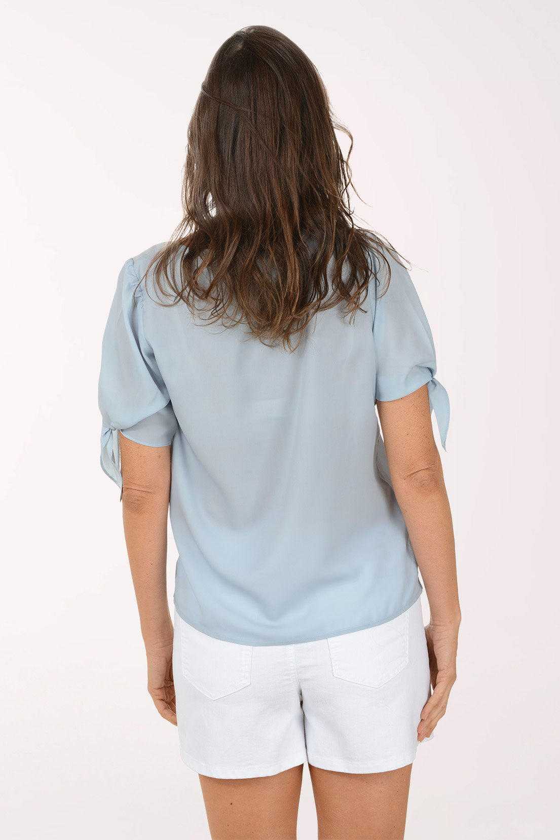 Woman wearing a light grey blouse with rolled-up sleeves and a white skirt on a white background