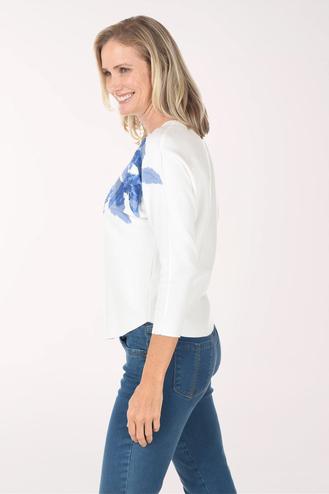 Woman wearing a white top with blue floral patterns on a plain background