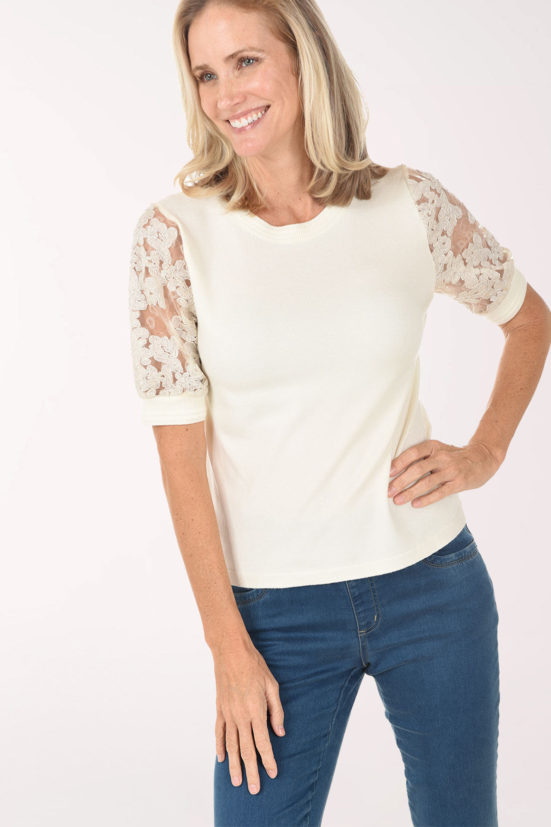 Woman wearing a white blouse with lace sleeves and blue jeans on a white background
