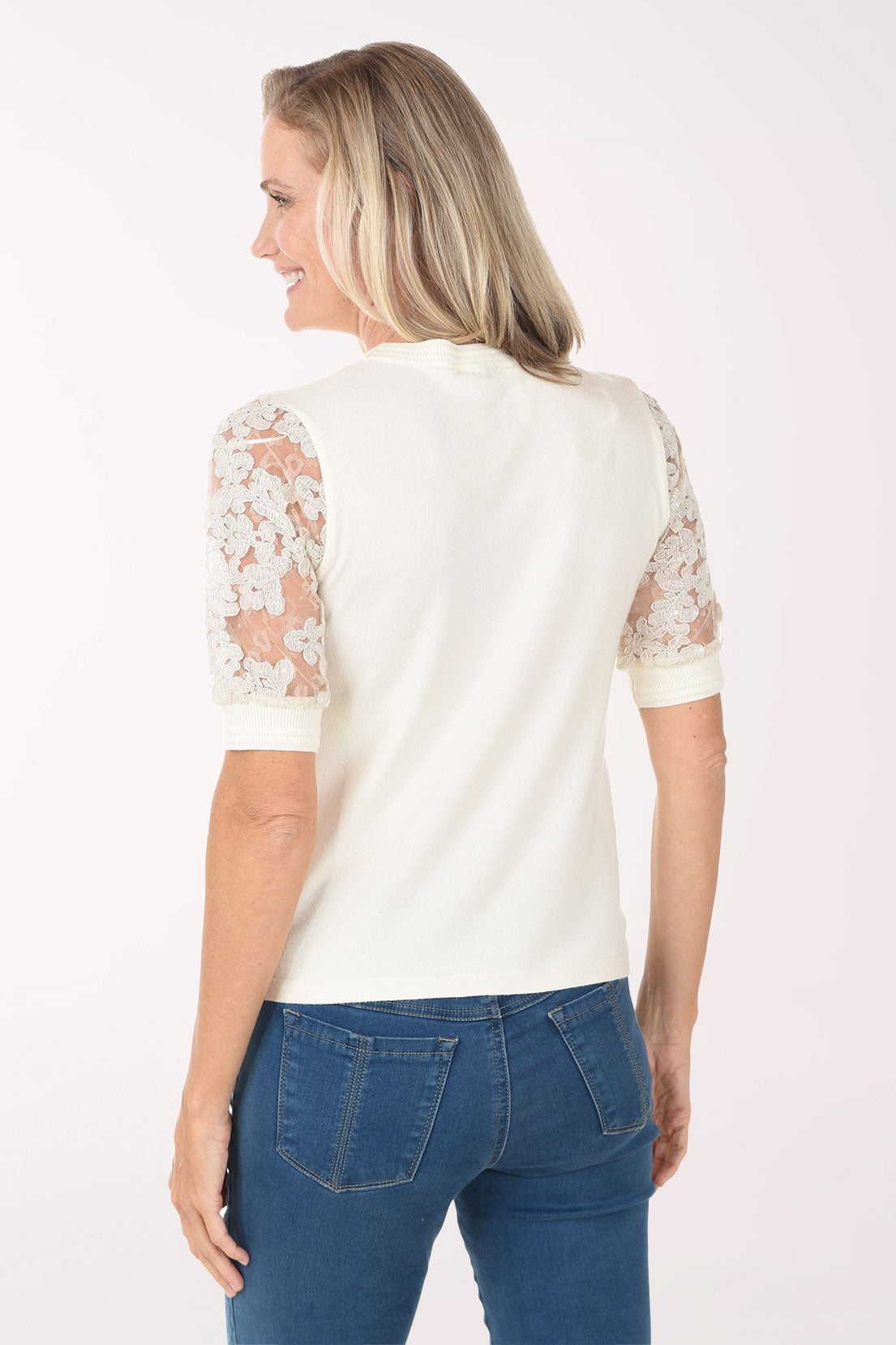 Woman wearing a white blouse with lace sleeves and blue jeans on a white background