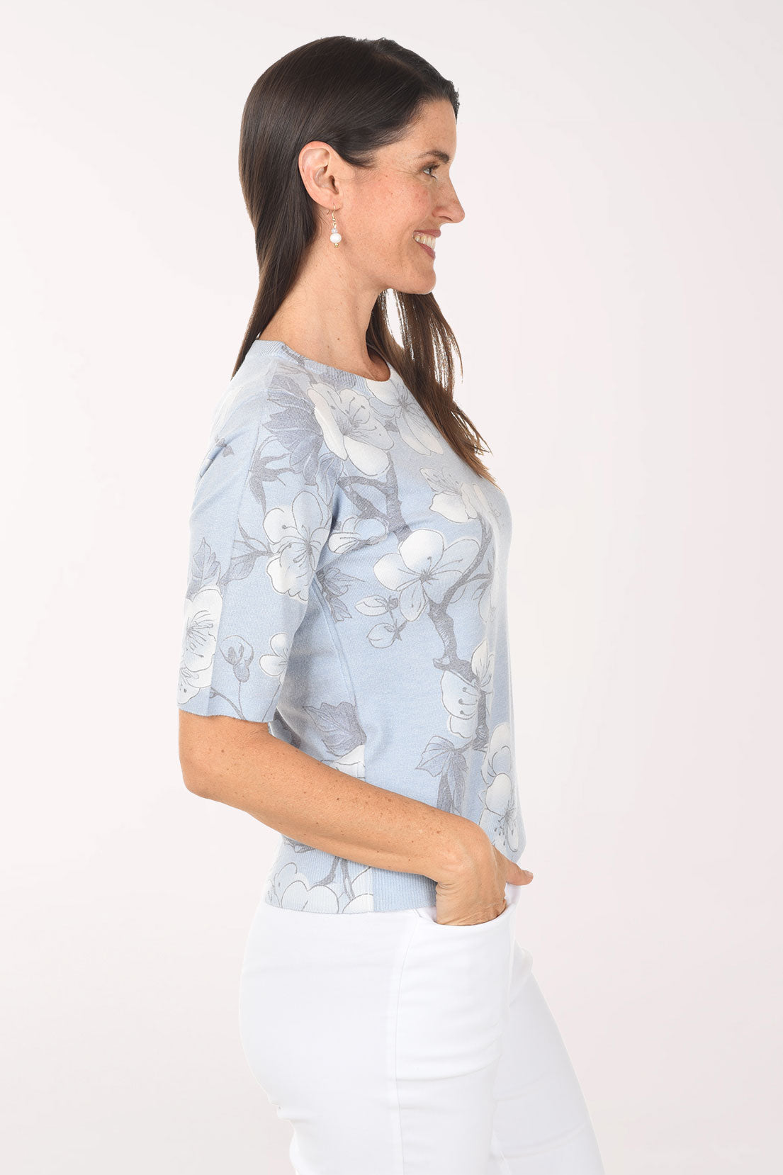 Woman wearing a light blue floral blouse with white pants on a white background