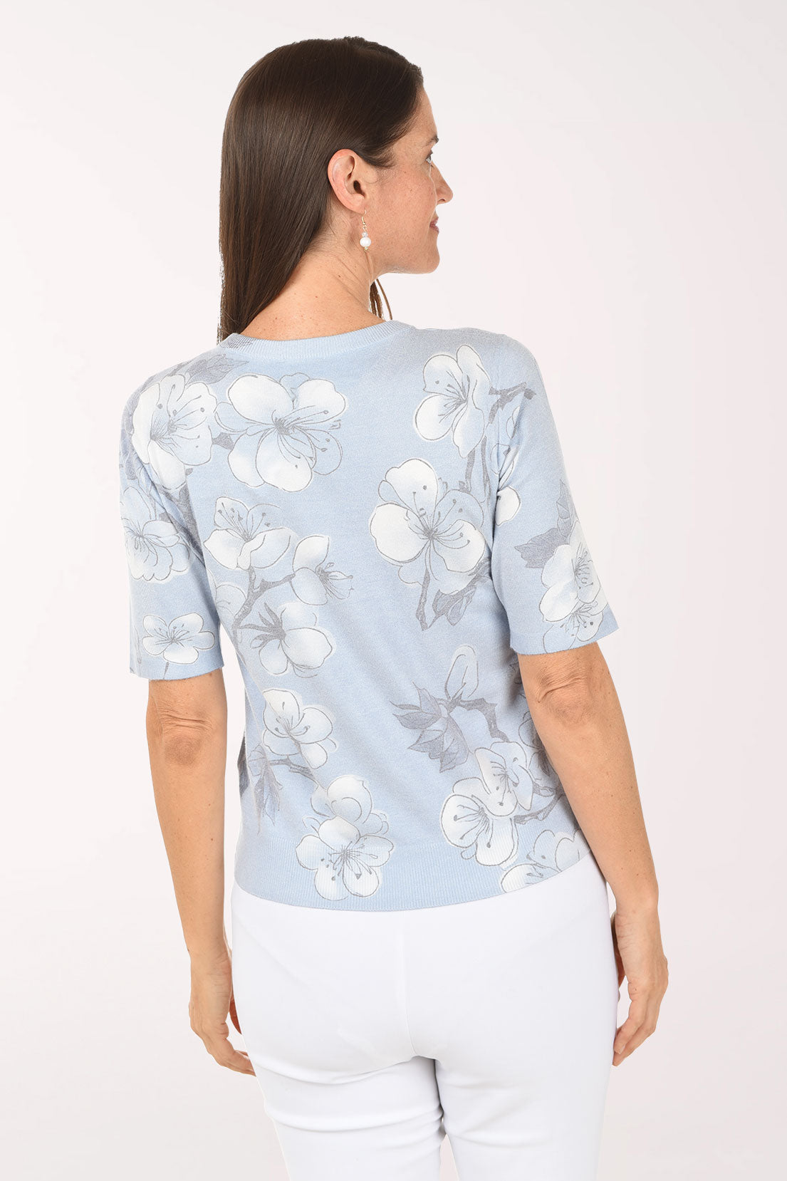 Woman wearing a light blue floral blouse with white pants on a white background