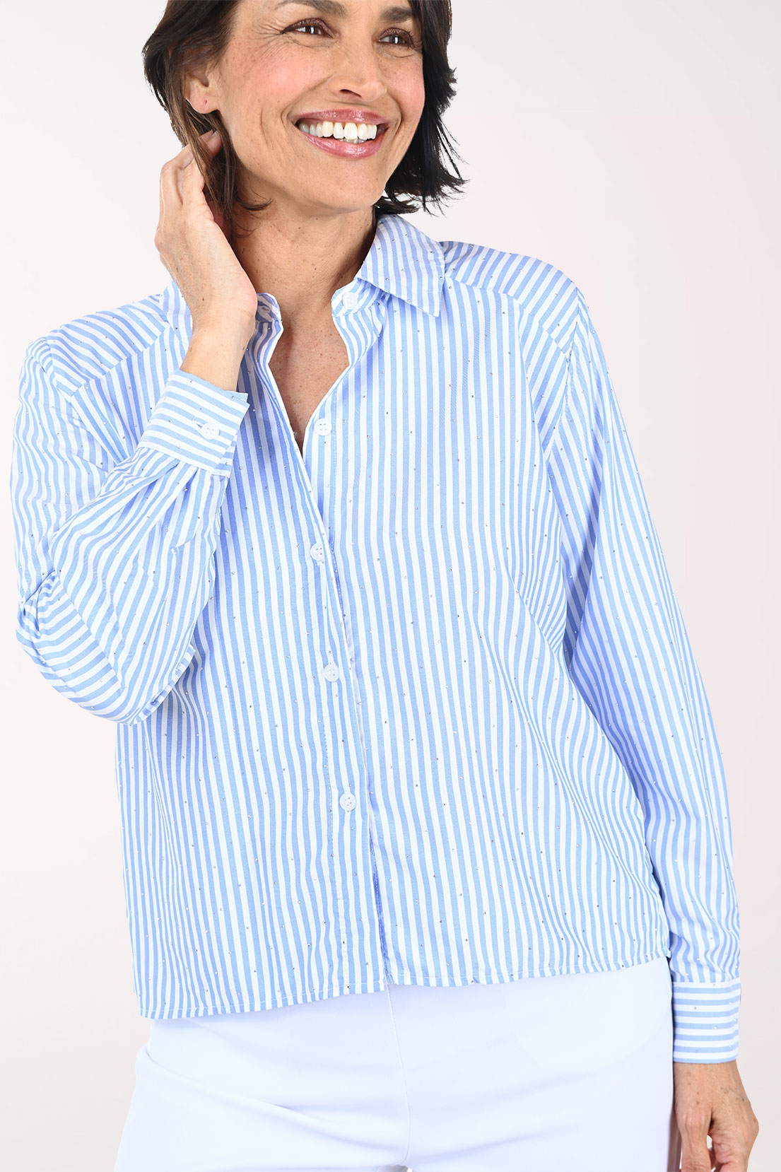 Woman wearing a light blue striped shirt and white pants on a plain background