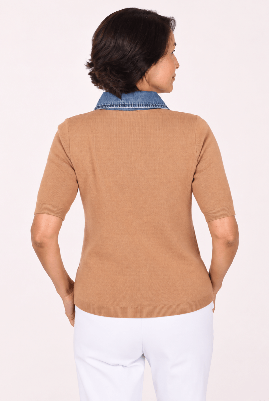 A woman shown from the back wearing a tan short-sleeve knit top with a blue denim collar, paired with white pants, against a plain light background.