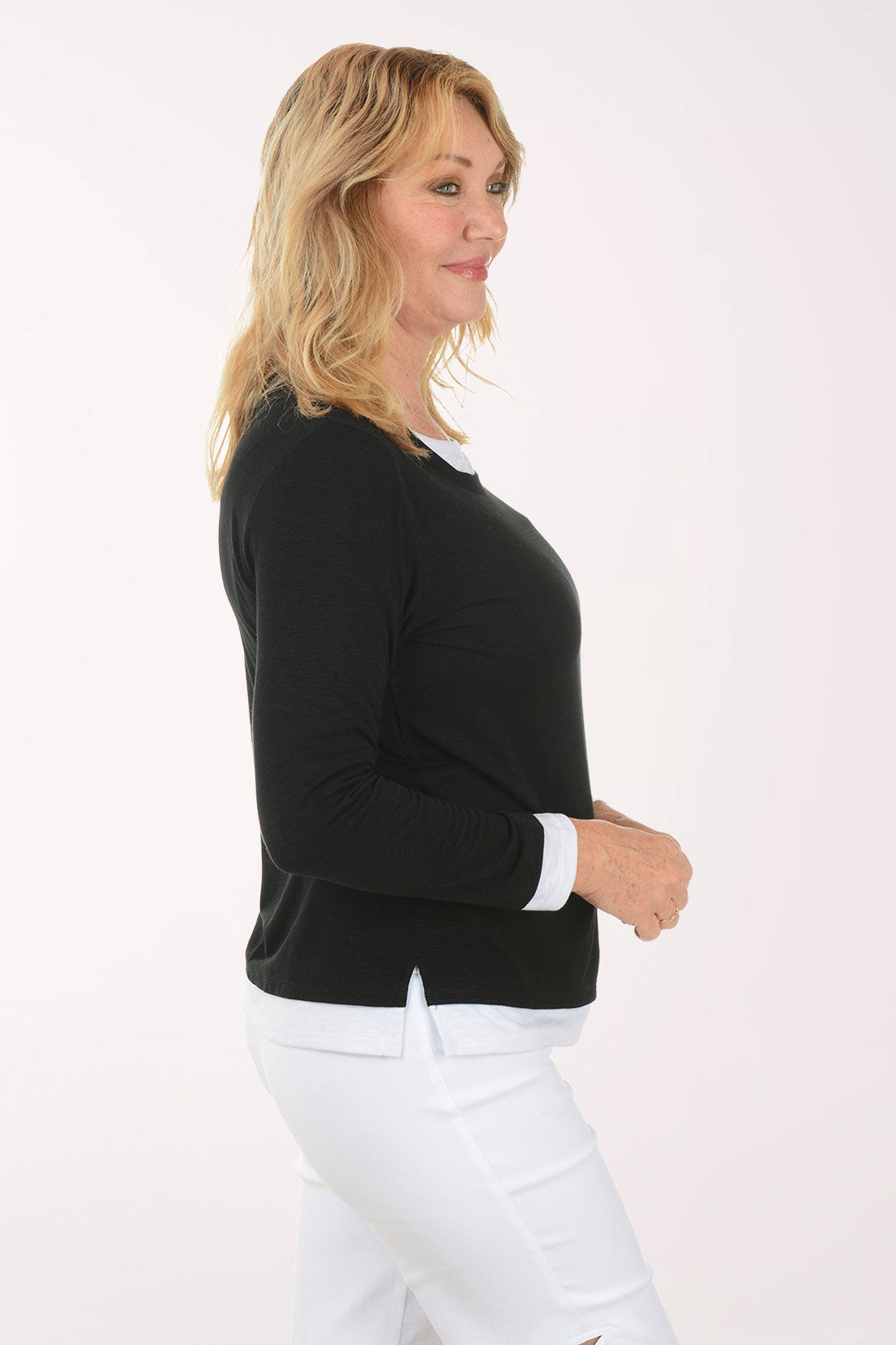 Woman wearing a black long-sleeve top and white pants on a white background