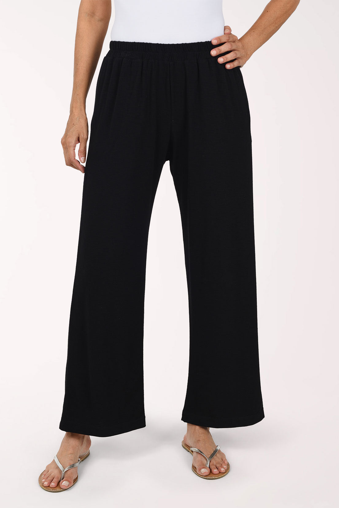 A person wearing black wide-leg pants with an elastic waistband and side pockets, paired with a white top and flat sandals, photographed against a plain light background.