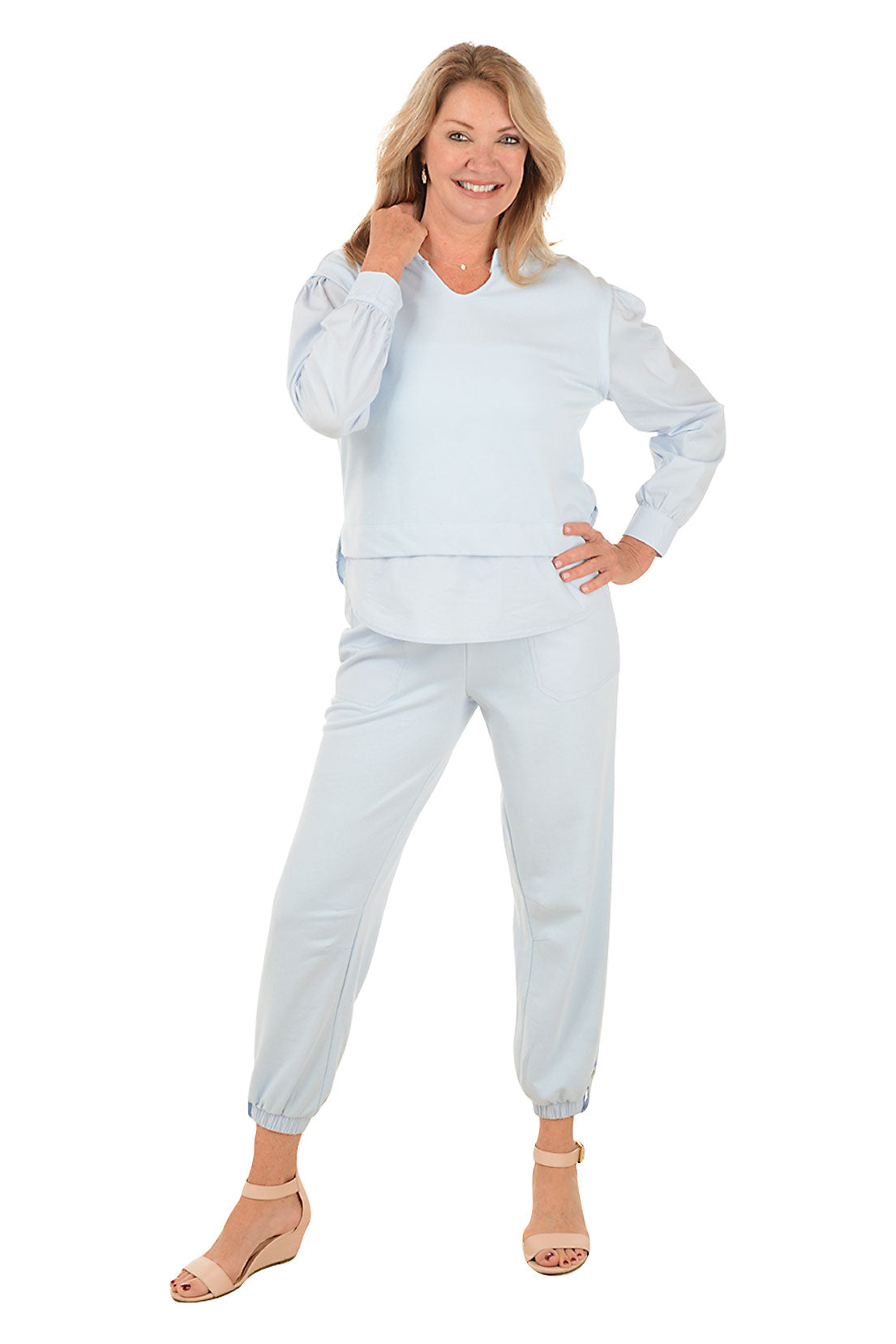 A full length shot of a model wearing a ankle-length light blue jogger pants with an elastic waistband, drawstring, and button tab detail at the ankles, featuring dual front patch pockets.