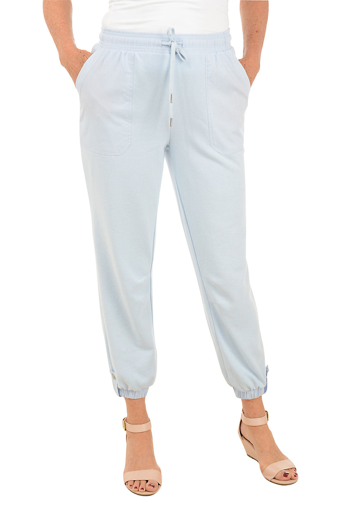A front shot of a model wearing a ankle-length light blue jogger pants with an elastic waistband, drawstring, and button tab detail at the ankles, featuring dual front patch pockets.