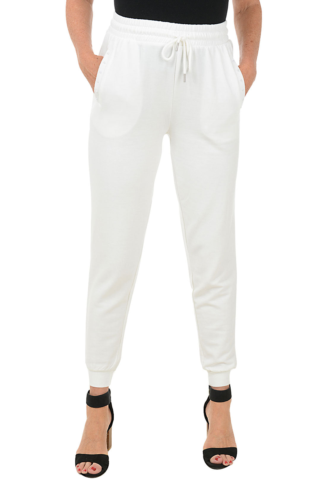 A front shot of a model wearing a pair of white jogger pants with an elastic waistband, adjustable drawstring, and faux pearl embellishment on the front pockets. The pants feature a ribbed cuff on the hemline and are flat-backed.