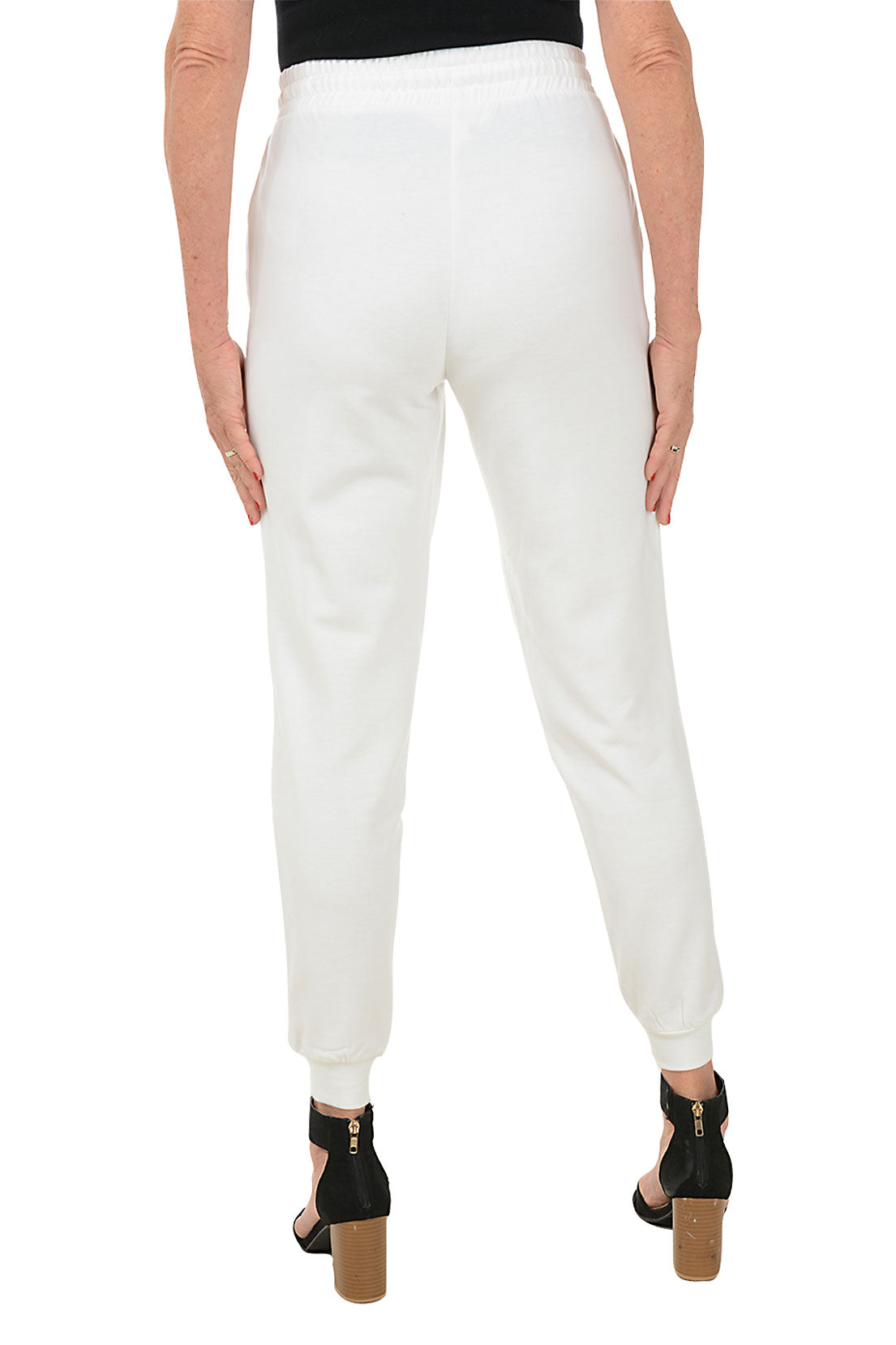 A back shot of a model wearing a pair of white jogger pants with an elastic waistband, adjustable drawstring, and faux pearl embellishment on the front pockets. The pants feature a ribbed cuff on the hemline and are flat-backed.
