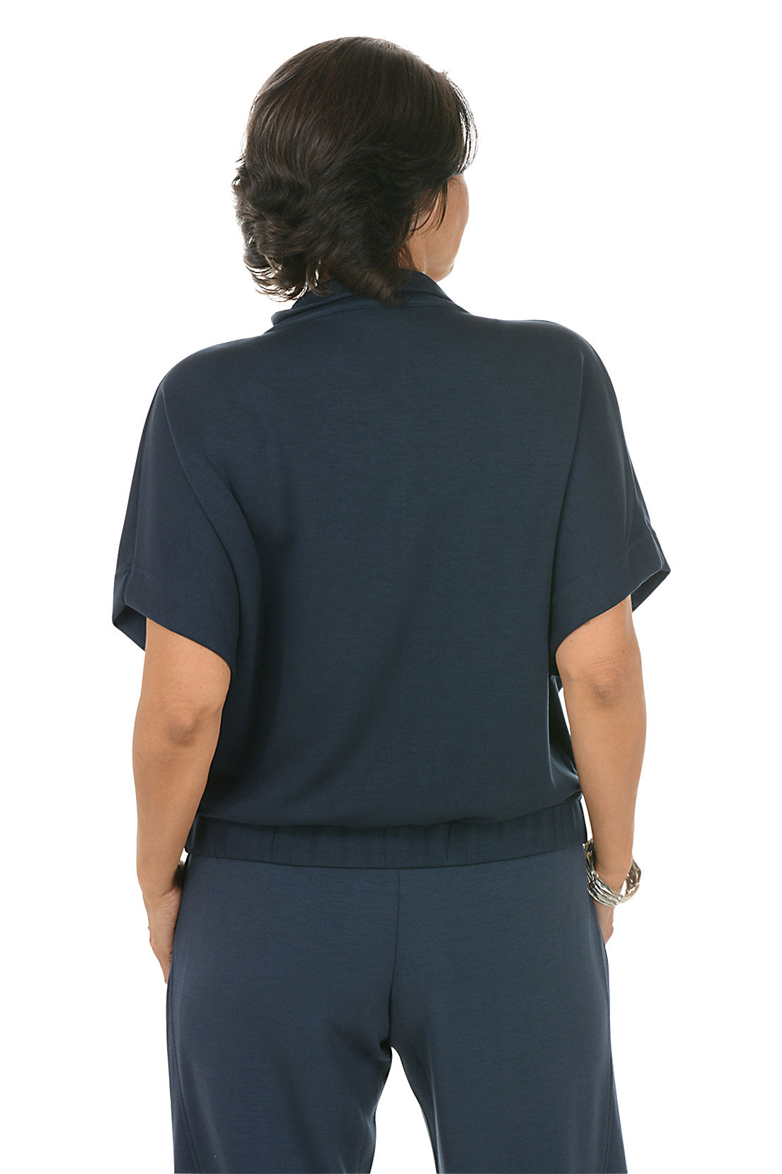 Woman wearing a navy blue zip-up top with a white background. Back shot.