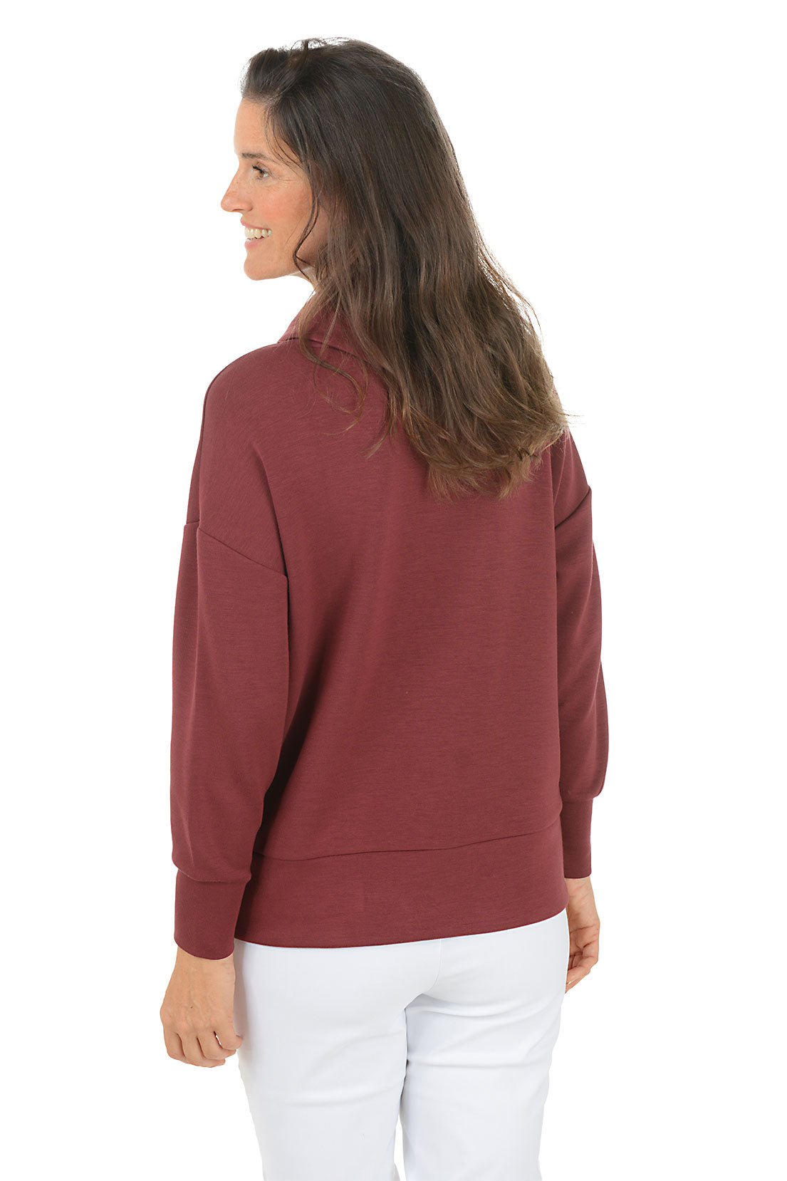 Woman wearing a maroon cowl-neck sweater and white pants on a white background. Back shot.