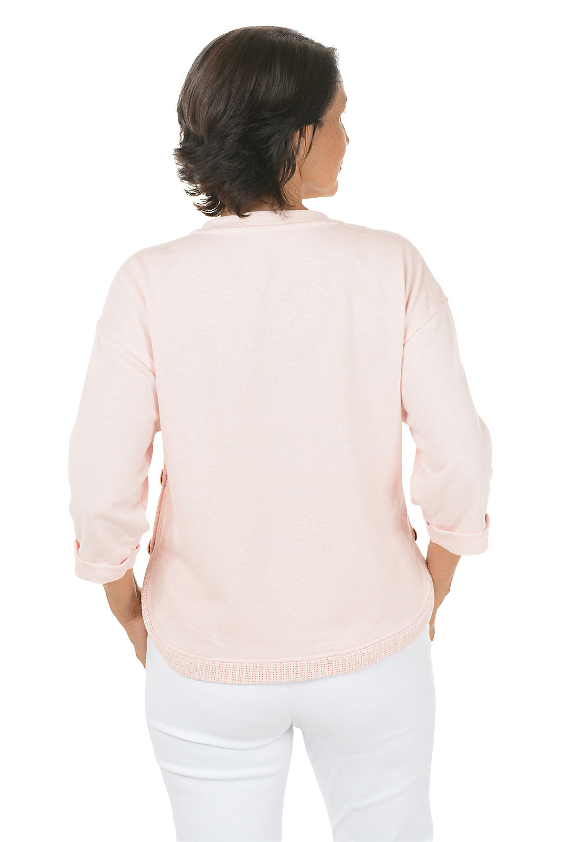 Woman wearing a light pink sweater and white pants on a white background. Back shot.
