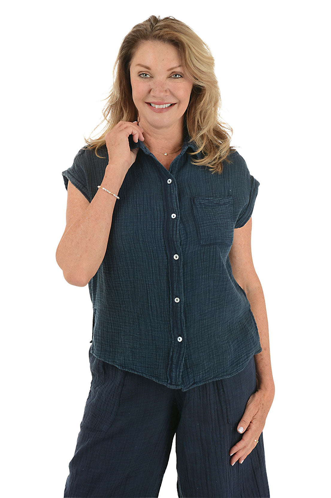A front shot of a model wearing a indigo button-front shirt with short dolman sleeves, a collar, and a left chest pocket. The shirt has a high-low hemline with side slits and she is also wearing blue jeans.