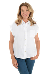 A front shot of a model wearing a white button-front shirt with short dolman sleeves, a collar, and a left chest pocket. The shirt has a high-low hemline with side slits and she is also wearing blue jeans.