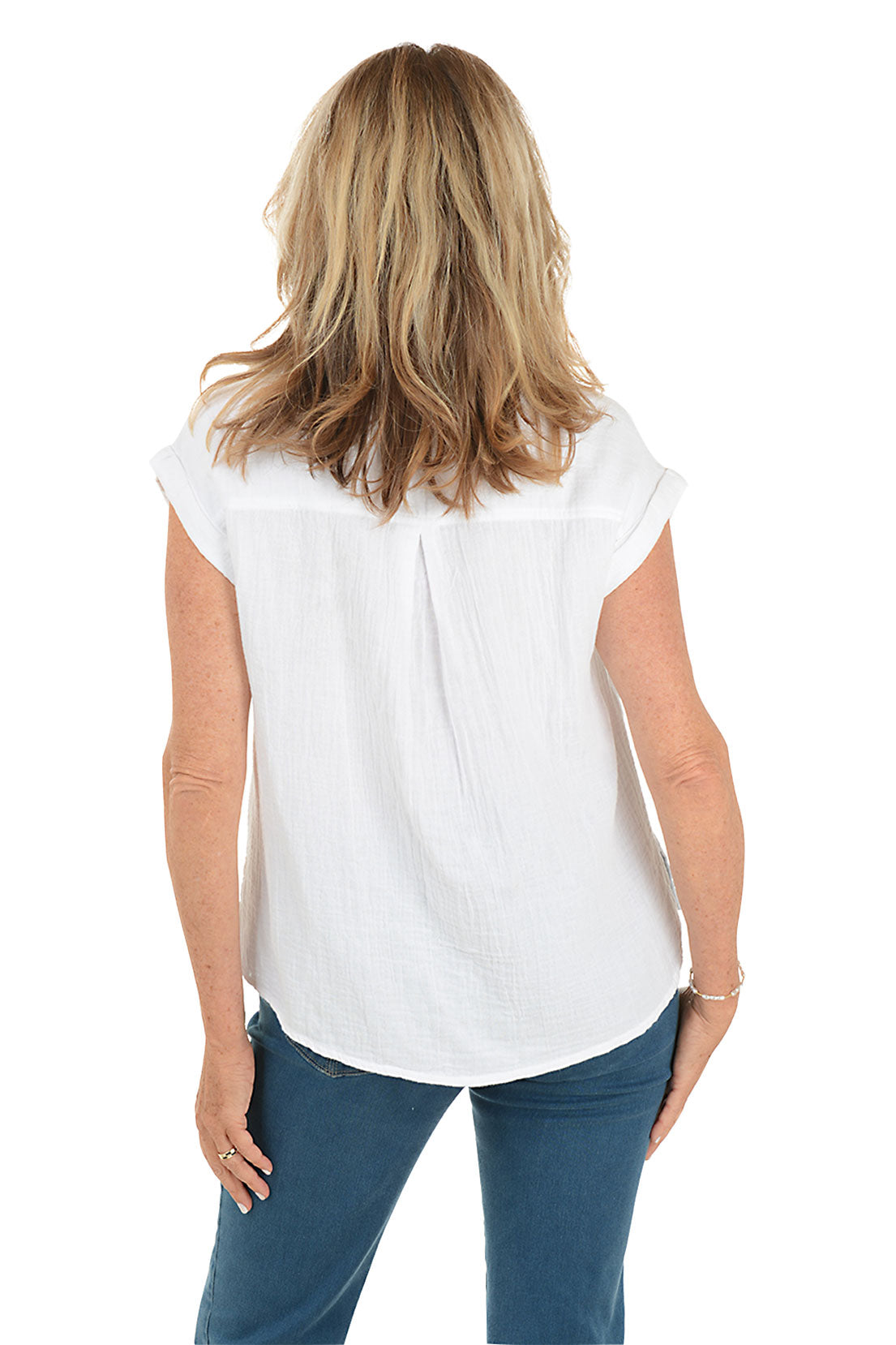 A back shot of a model wearing a white button-front shirt with short dolman sleeves, a collar, and a left chest pocket. The shirt has a high-low hemline with side slits and she is also wearing blue jeans.