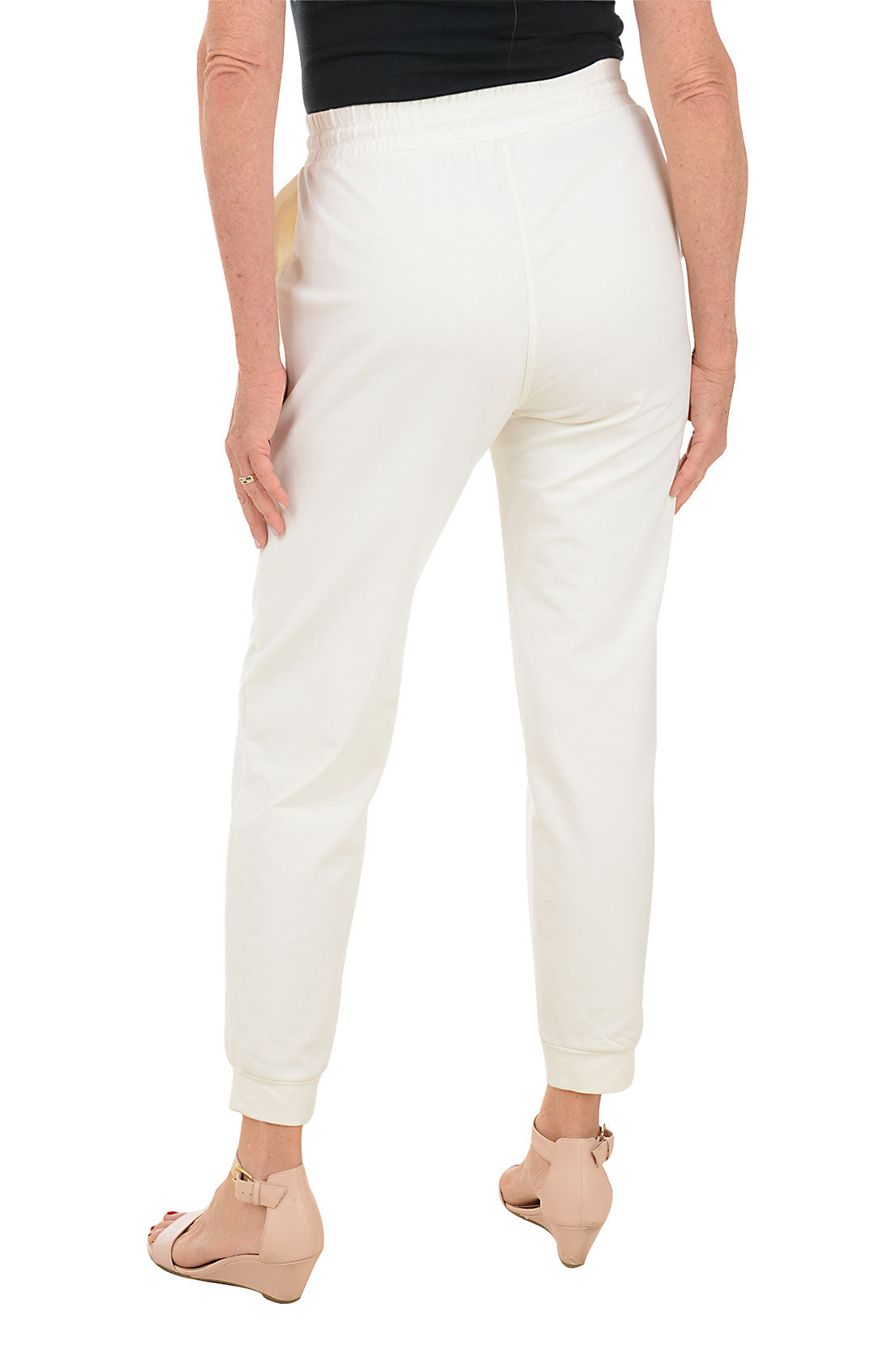 A back shot of a model wearing a ankle-length white jogger pants with a drawstring waistband, dual front pockets, and an ankle cuff. The pants are made of French terry fabric.