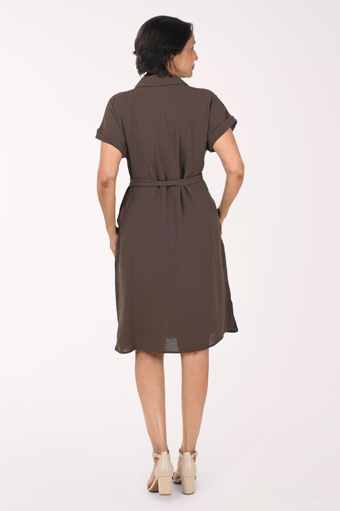 A woman modeling a brown short-sleeve shirt dress with a tie waist, standing against a plain white studio background.