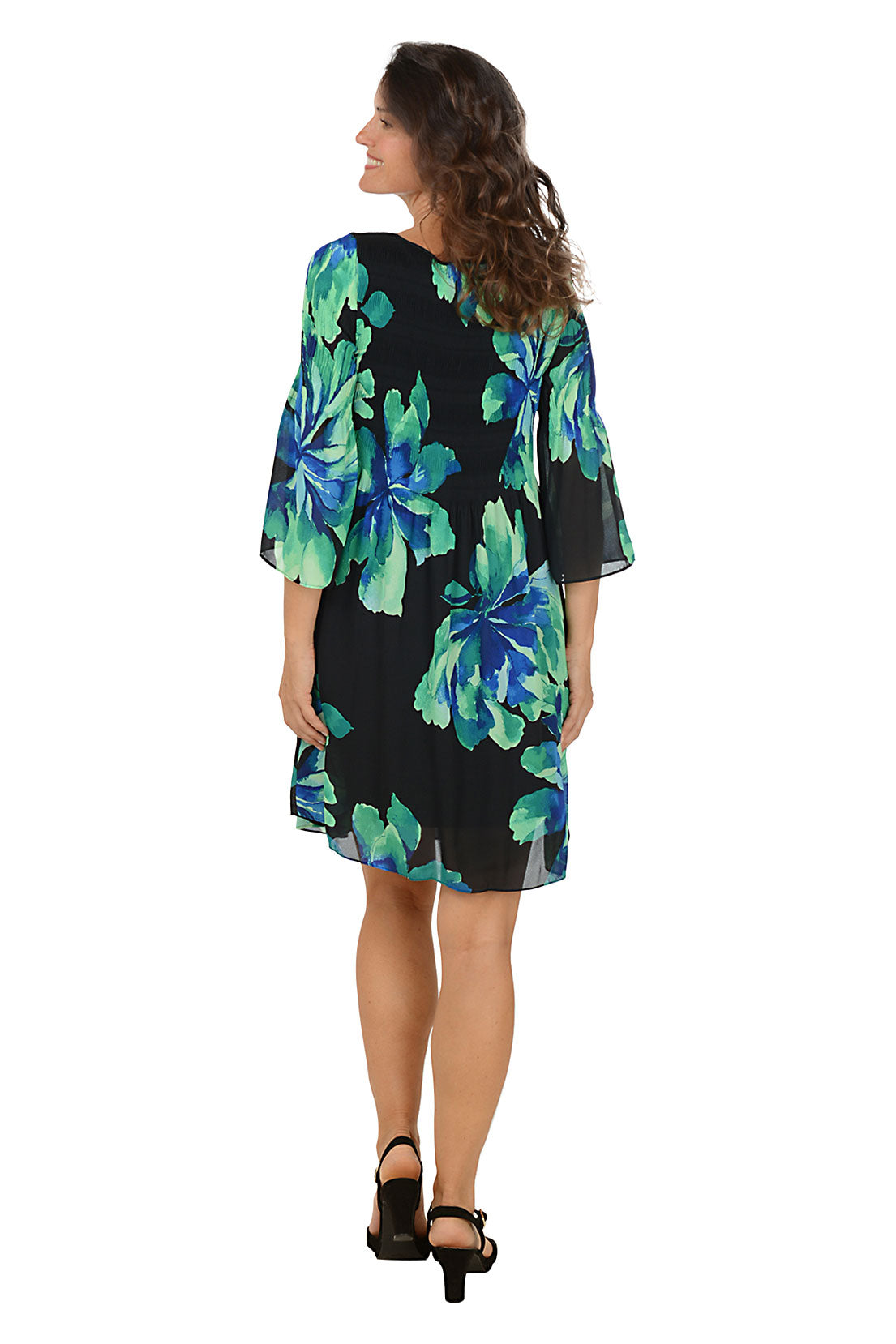 Woman wearing a black dress with blue and green floral pattern on a white background. Back shot.