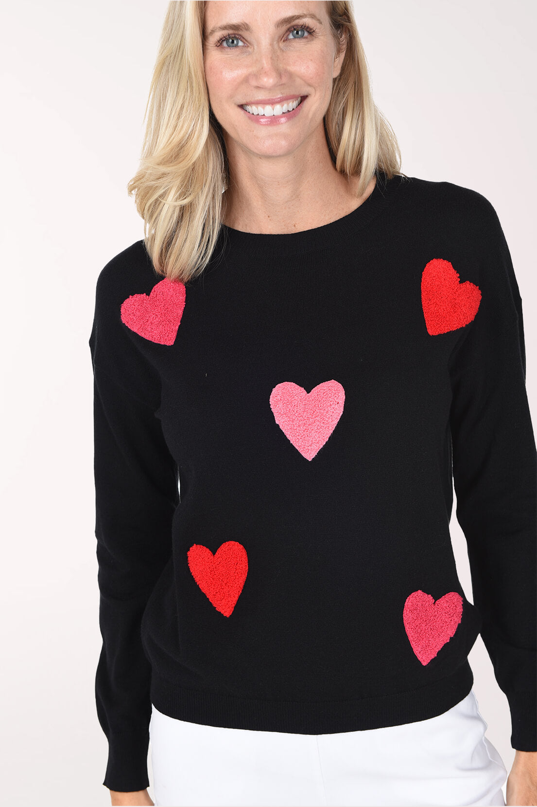 Model wearing a black sweater featuring a playful red and pink heart pattern.