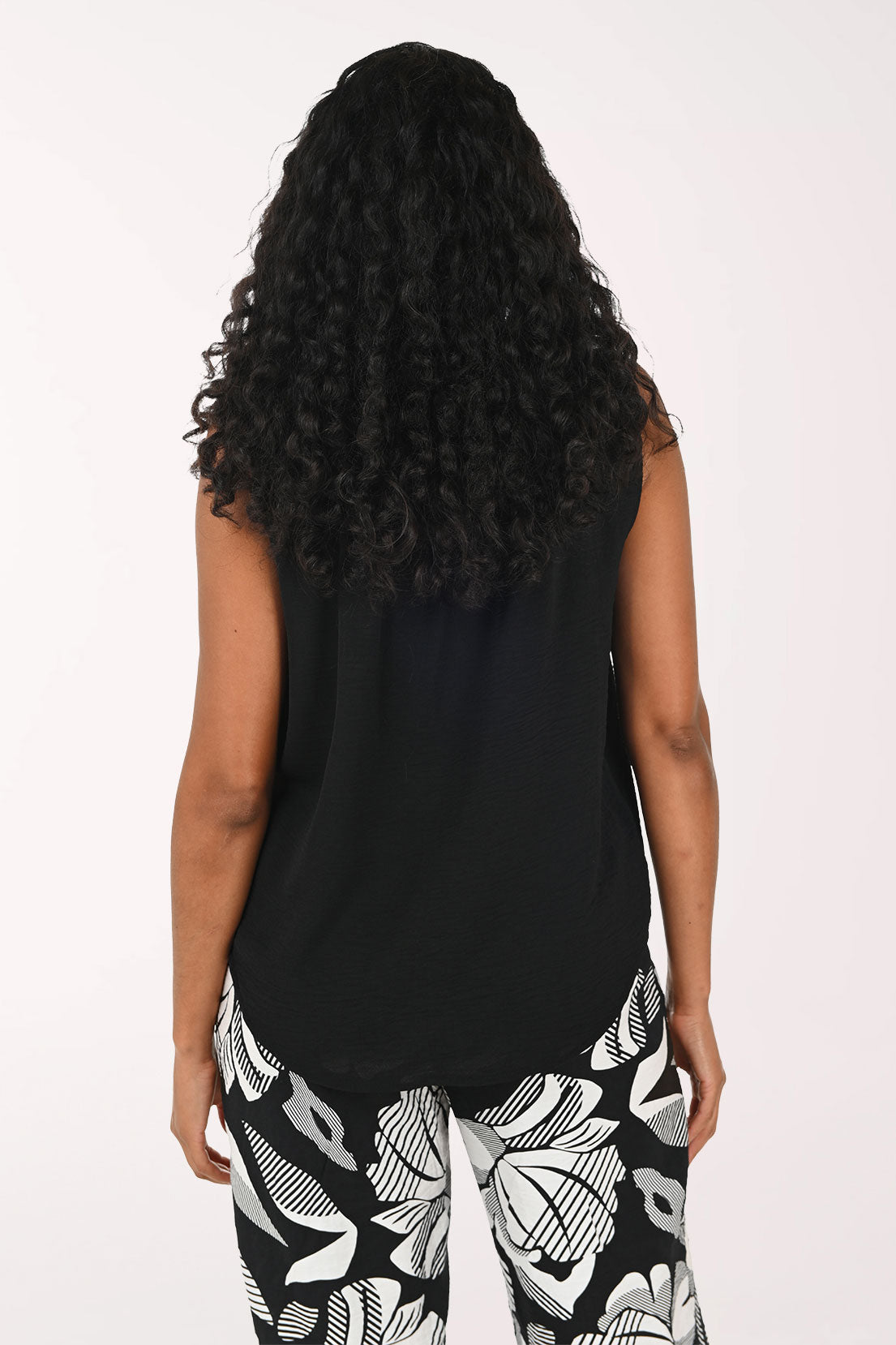 Woman wearing a black sleeveless top and patterned pants on a white background