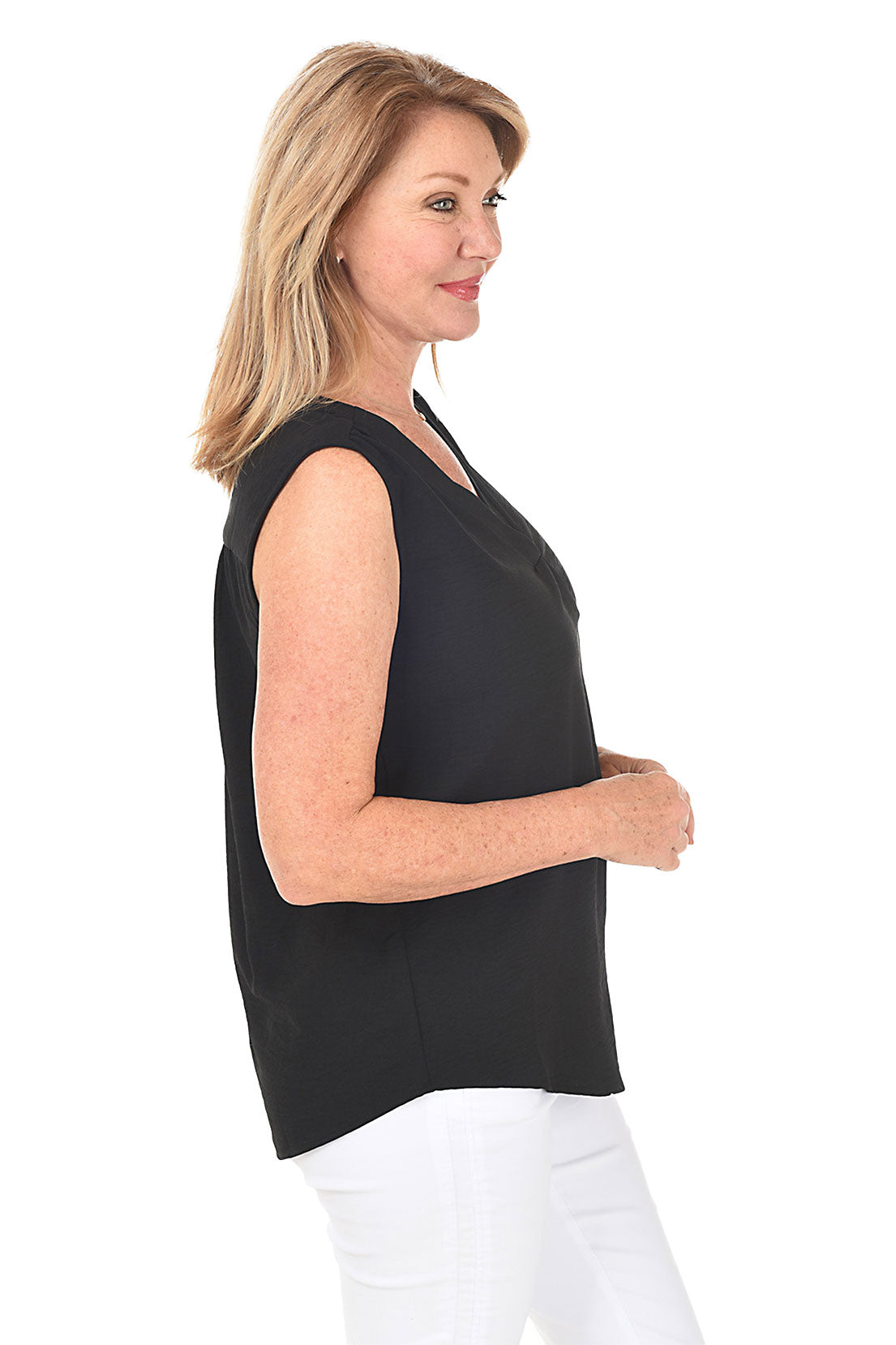 A side shot of a model wearing a sleeveless black blouse with a V-neckline and a center front inverted pleat, paired with white pants.