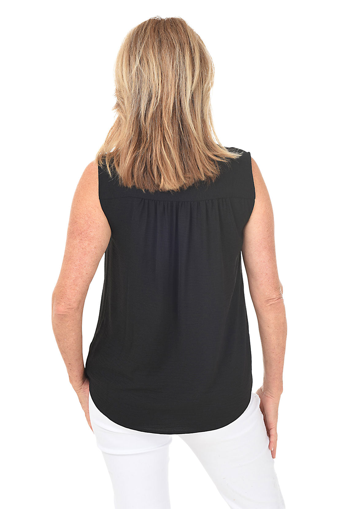 A back shot of a model wearing a sleeveless black blouse with a V-neckline and a center front inverted pleat, paired with white pants.