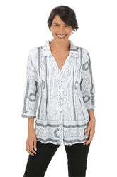 A front shot of a model wearing a pleated button-front shirt with a foldover collar, 3/4 sleeves with cuffs, and a flared hemline. The shirt is printed with a geometric pattern and the person is smiling.