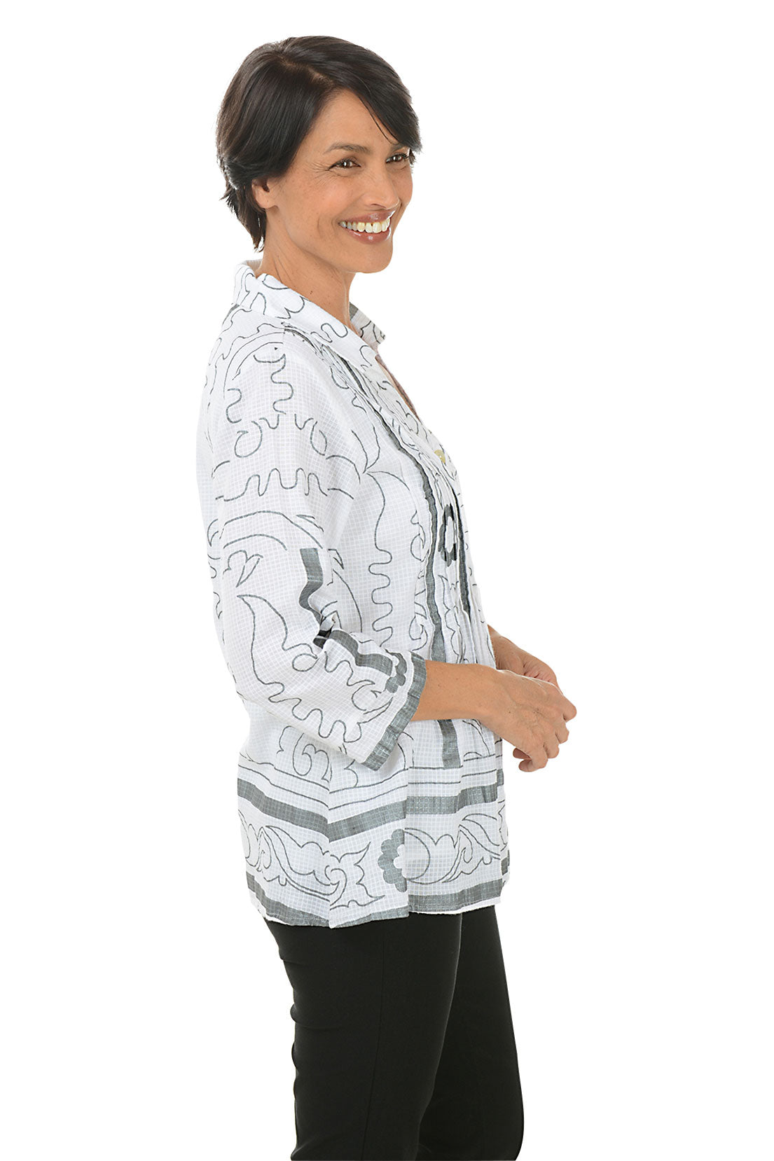 A side shot of a model wearing a pleated button-front shirt with a foldover collar, 3/4 sleeves with cuffs, and a flared hemline. The shirt is printed with a geometric pattern and the person is smiling.