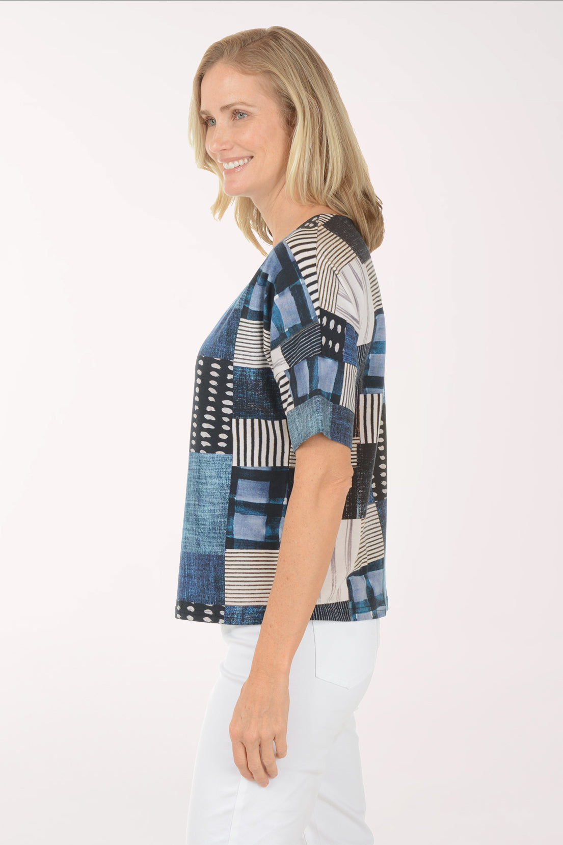 Woman wearing a patchwork top with blue, black, and white patterns on a white background
