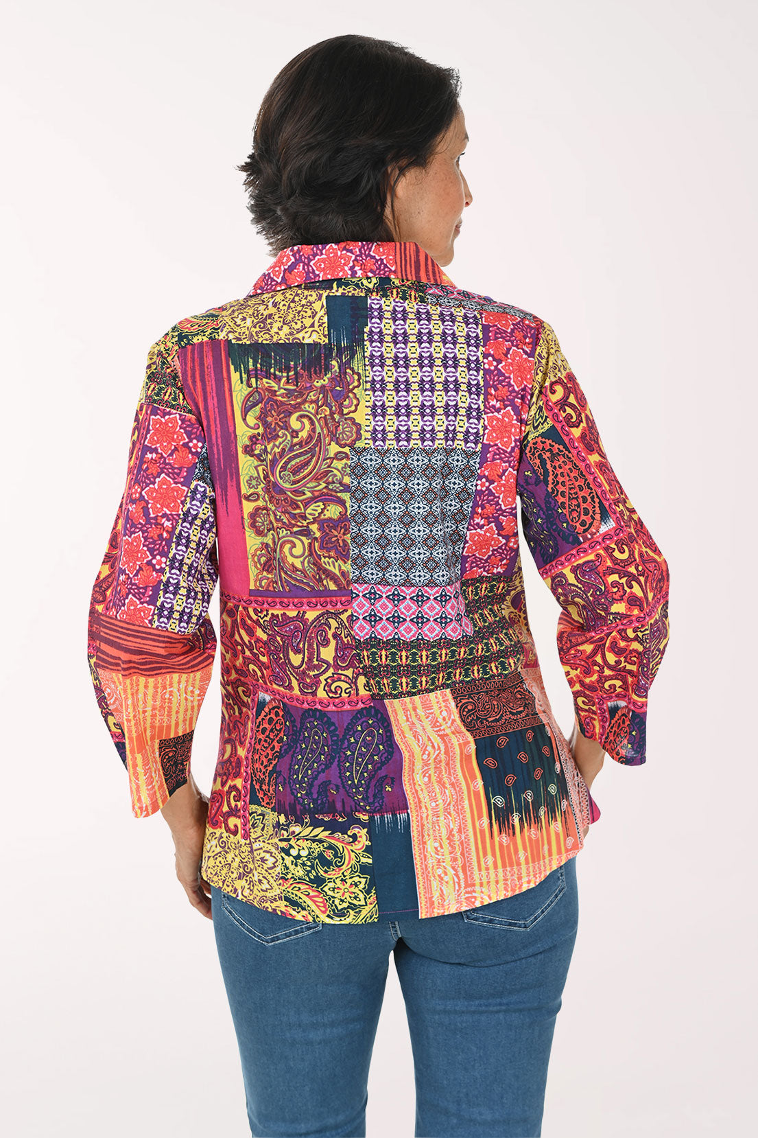 A woman modeling a vibrant, multicolored patchwork button-up shirt with intricate botanical and geometric patterns, paired with blue jeans against a plain white background.