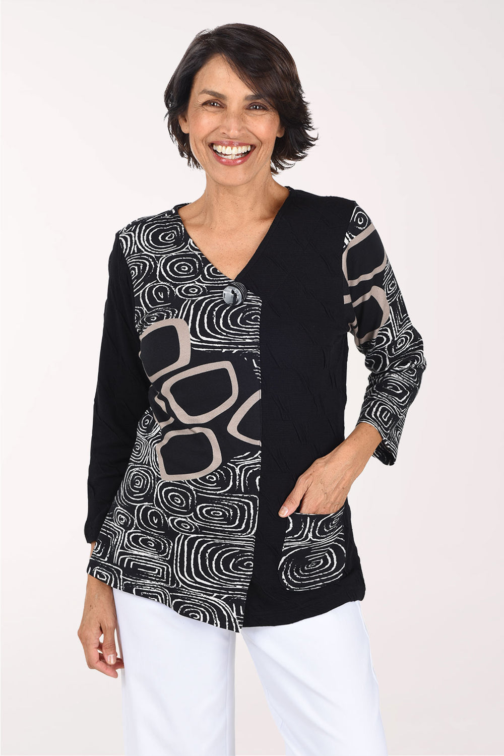 Woman wearing a 3/4 sleeve black top with an abstract pattern on half of the top, one arm, and pocket.