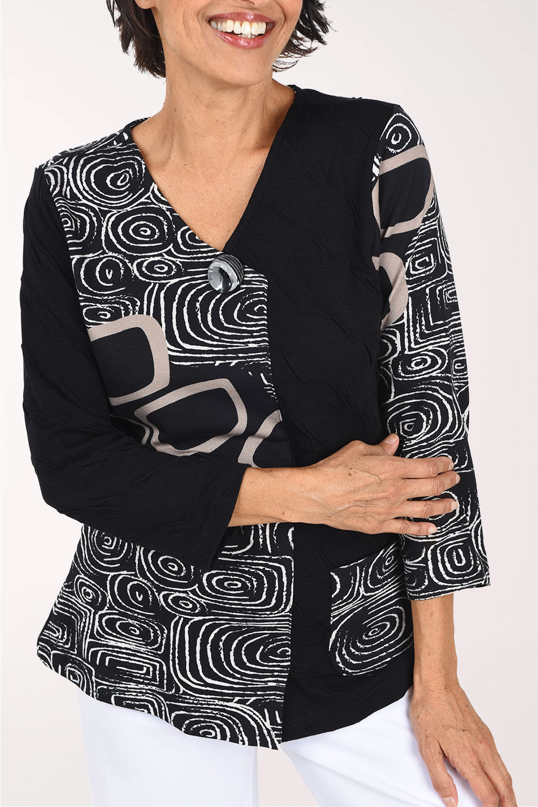 Woman wearing a 3/4 sleeve black top with an abstract pattern on half of the top, one arm, and pocket.