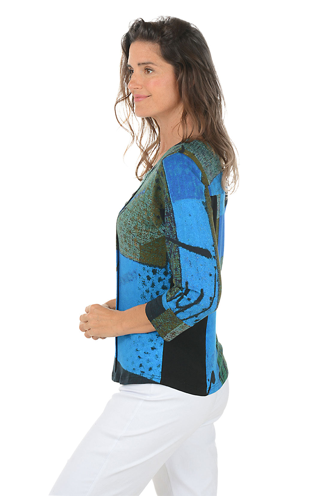 Woman wearing a colorful patterned top with blue and green design on a white background. Side shot.