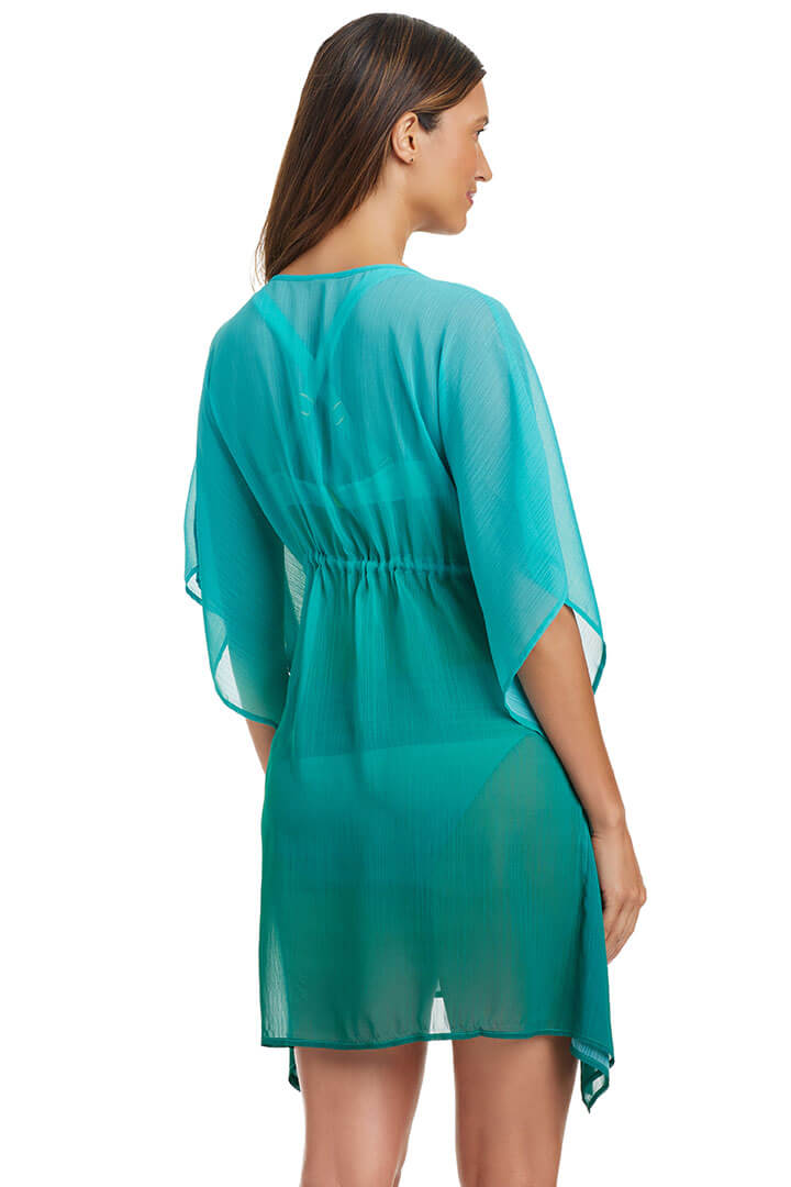 A woman wearing a teal blue deep v-neck caftan with kimono sleeves and a tasseled drawstring on the waistline. Back shot.
