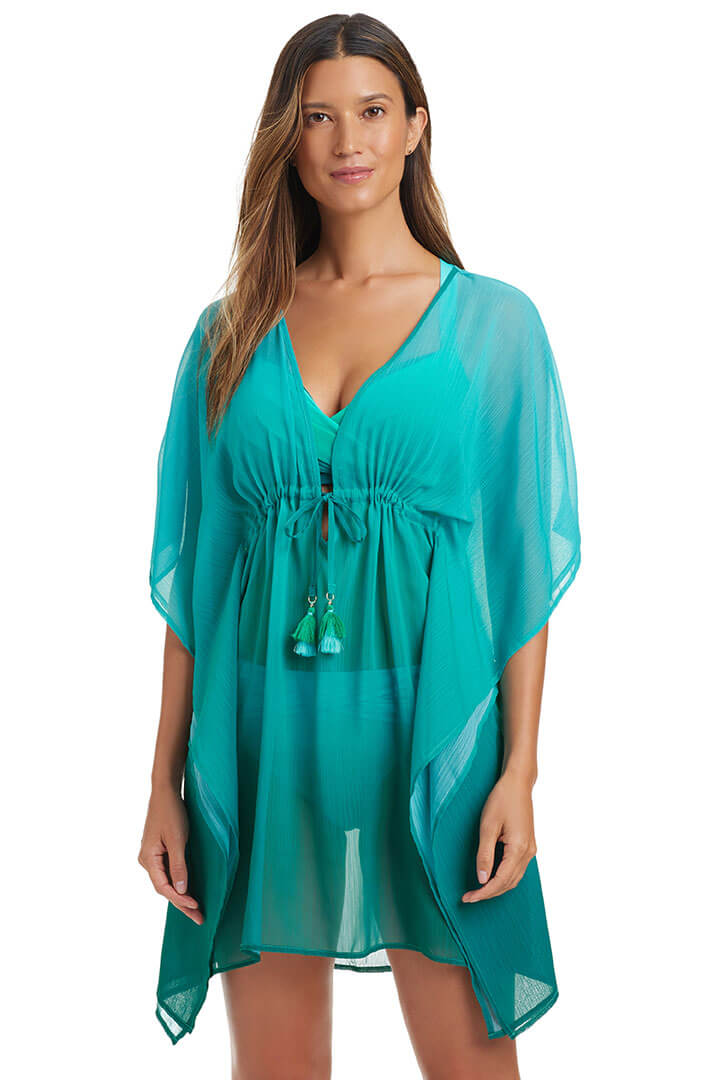 A woman wearing a teal blue deep v-neck caftan with kimono sleeves and a tasseled drawstring on the waistline.