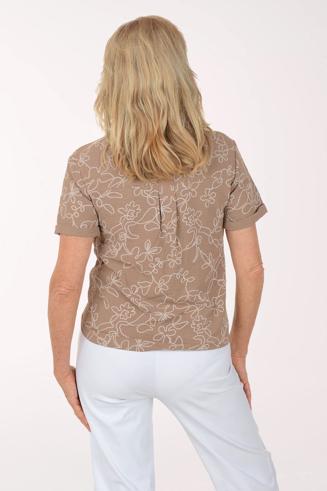 Woman wearing a patterned brown shirt and white pants on a white background
