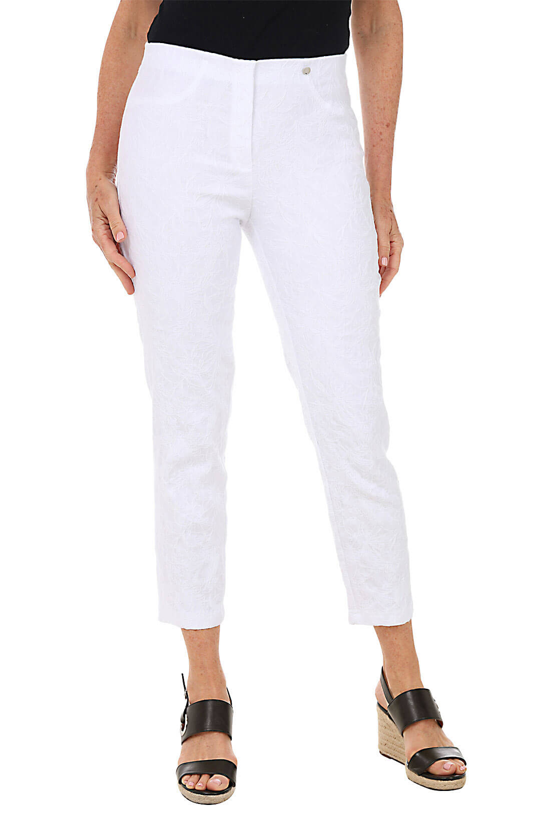 A front shot of a model wearing a pair of white floral jacquard pull-on ankle pants with faux front pockets and back patch pockets, standing against a plain background.