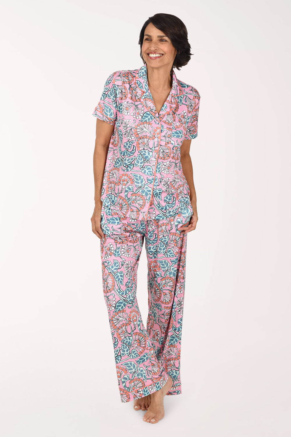 A woman modeling a matching short-sleeve button-front top and wide-leg pajama pants set with a pink, teal, and orange paisley pattern against a plain white studio background.