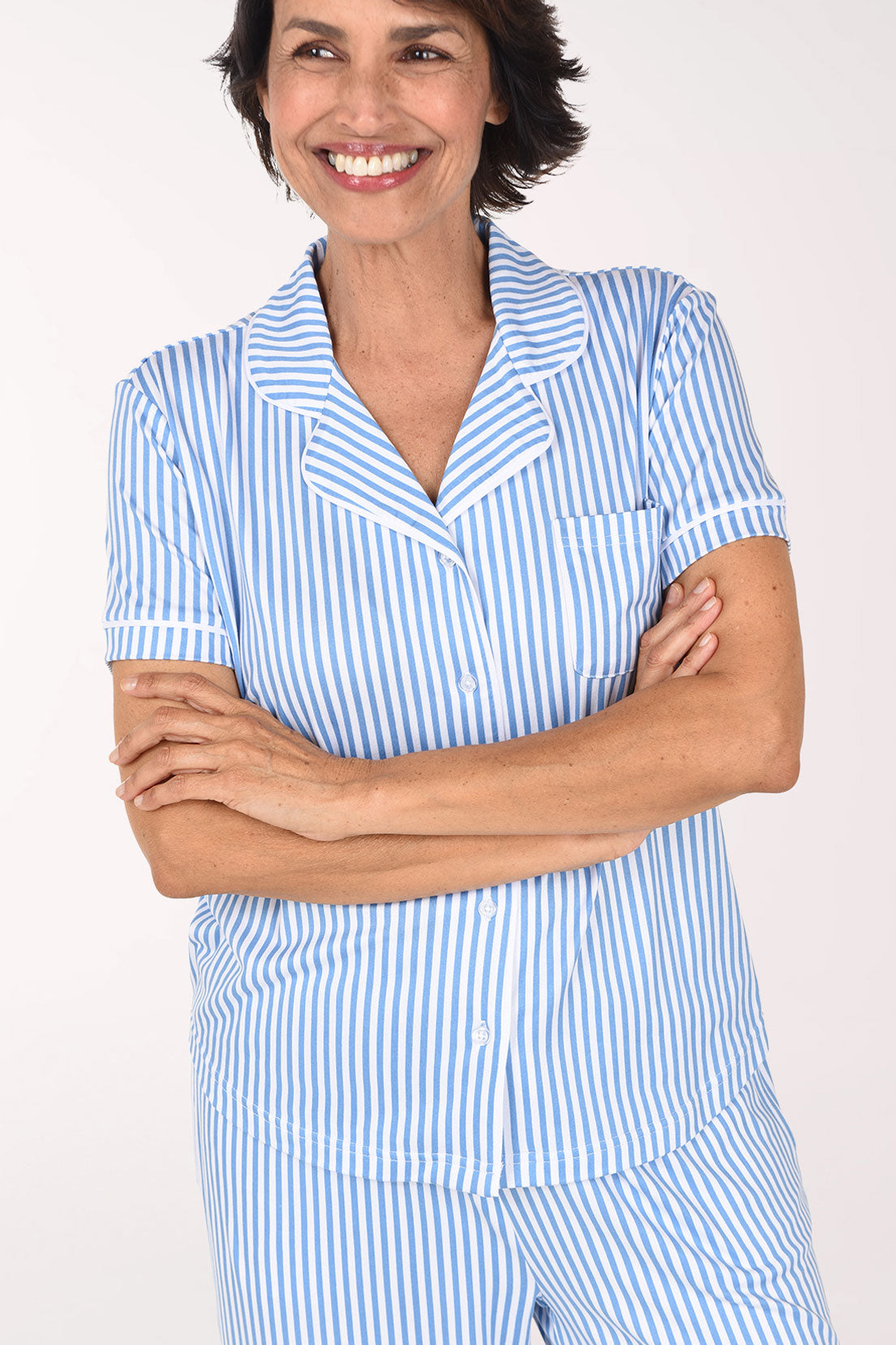 A woman smiling and posing in a light blue and white vertically striped short-sleeve pajama set against a plain white studio background.