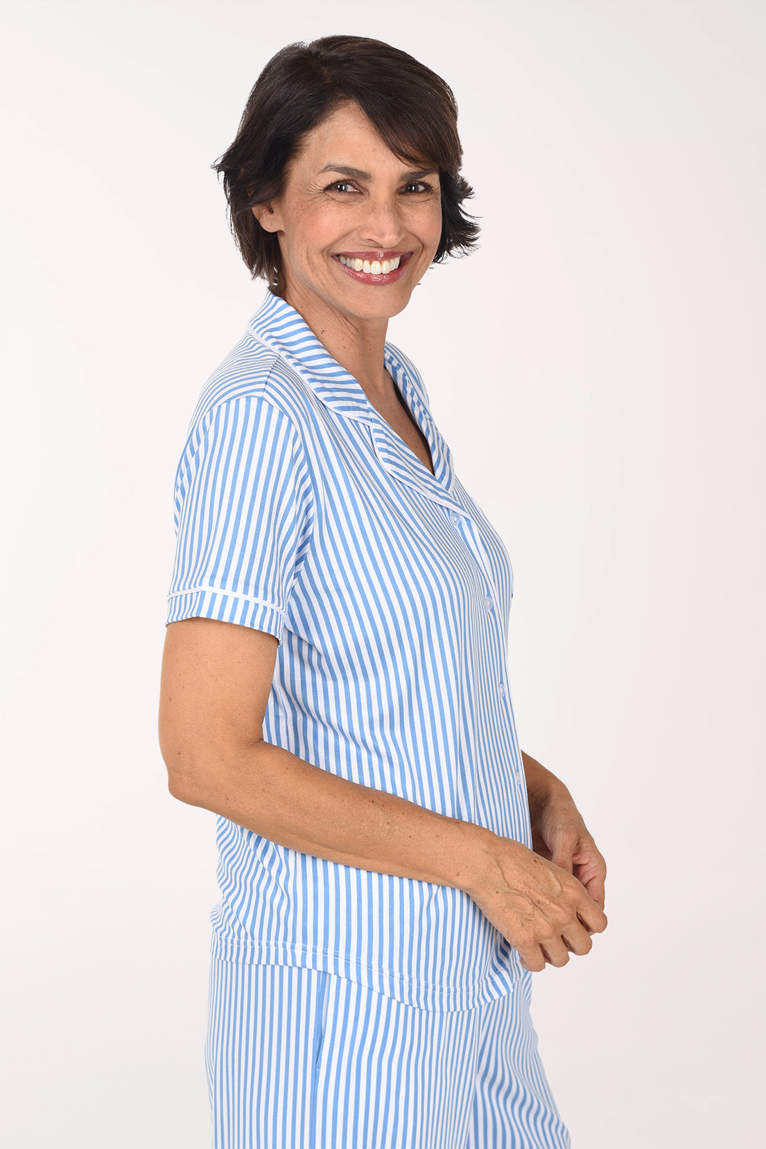 A woman smiling and posing in a light blue and white vertically striped short-sleeve pajama set against a plain white studio background.
