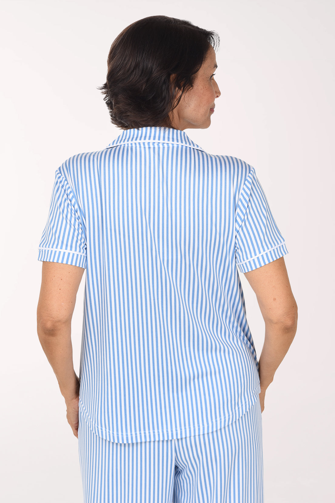 A woman smiling and posing in a light blue and white vertically striped short-sleeve pajama set against a plain white studio background.